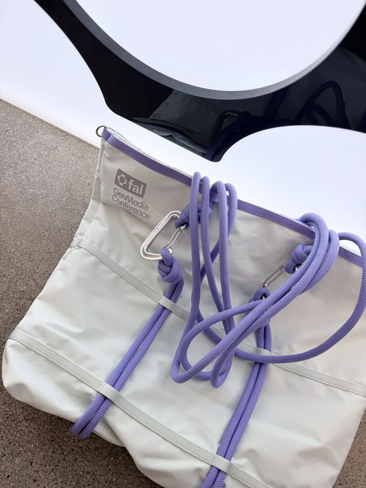 A light sage nylon tote with lavender rope straps, silver carabiners and a fal GenMedia Conference logo