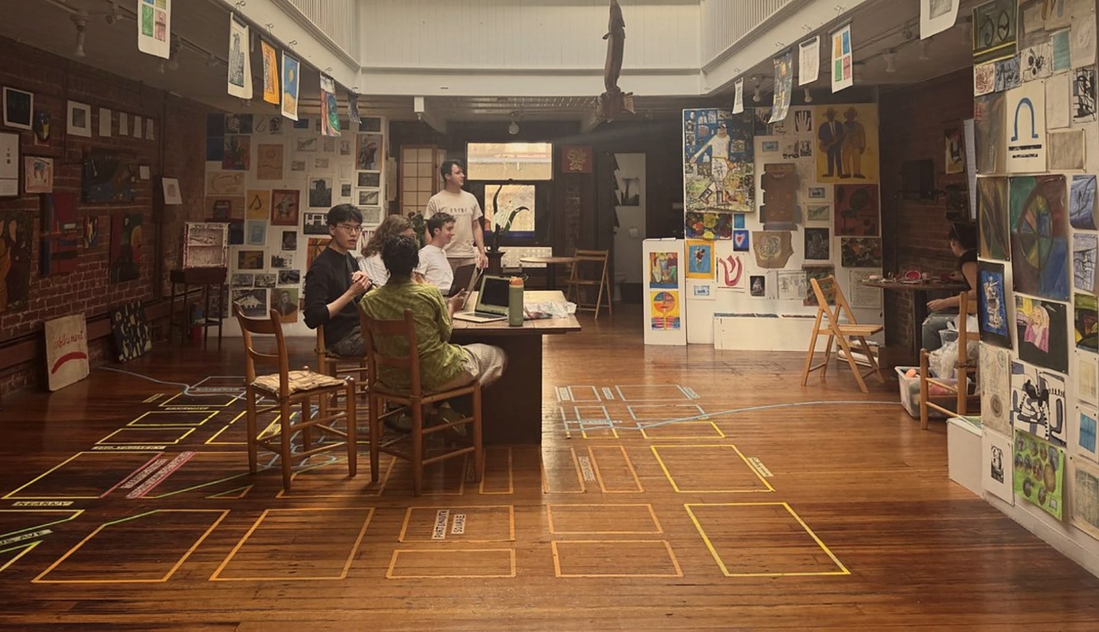 Era&rsquo;s team working at a long table in an art gallery, walls covered in paintings and the floor marked out with coloured tape